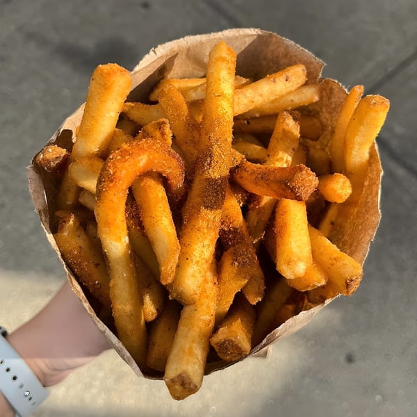 Hand holding a paper bag filled with golden-brown french fries seasoned with red spice.