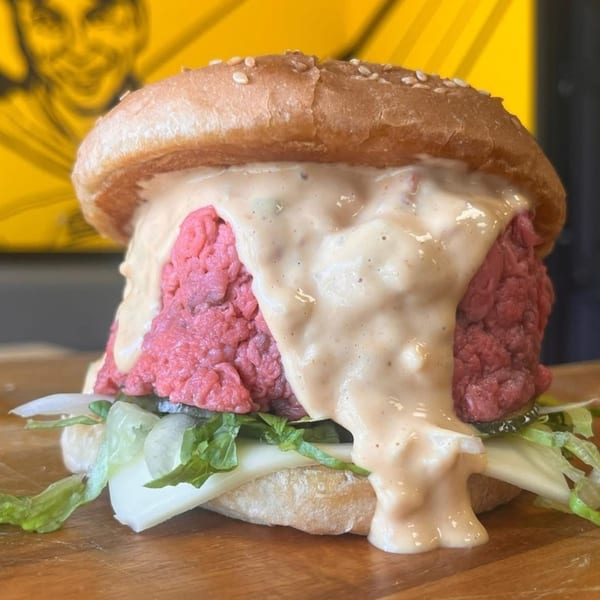 A large burger with a thick raw beef patty, melted cheese, lettuce, and special sauce.