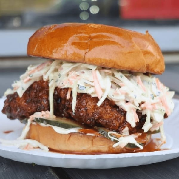 A crispy fried chicken sandwich with coleslaw and pickles on a brioche bun.