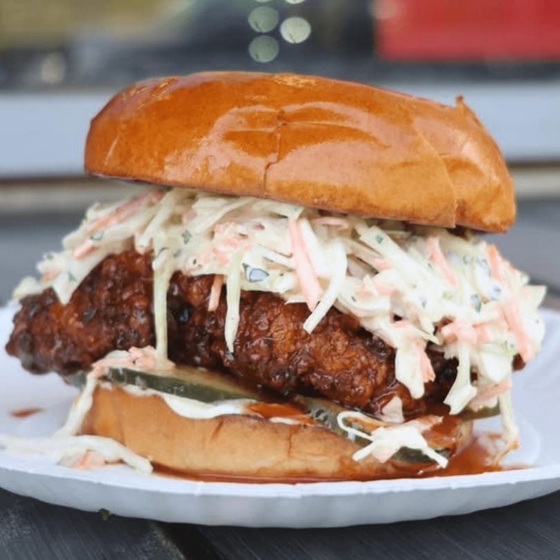 A crispy fried chicken sandwich with coleslaw and pickles on a brioche bun.