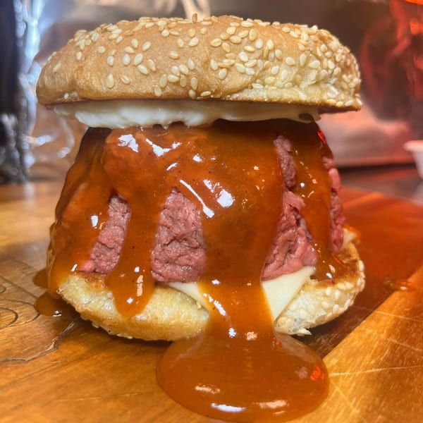 A messy roast beef sandwich with melted cheese and a generous amount of sauce dripping down.
