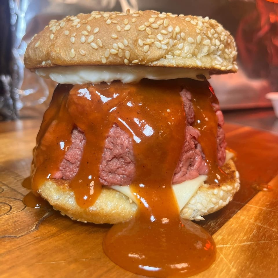 A messy roast beef sandwich with melted cheese and a generous amount of sauce dripping down.
