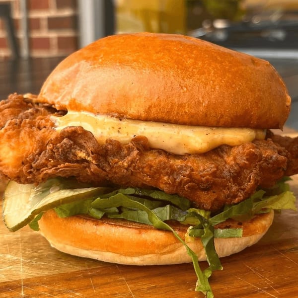 Crispy fried chicken sandwich with sauce, lettuce, and pickles on a brioche bun.