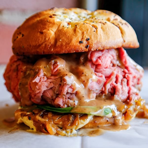 A close-up of a roast beef sandwich with gravy, caramelized onions, and green lettuce.